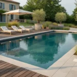 Piscine à débordement avec terrasse en bois exotique, dalles minérales et massifs d'oliviers dans un jardin
